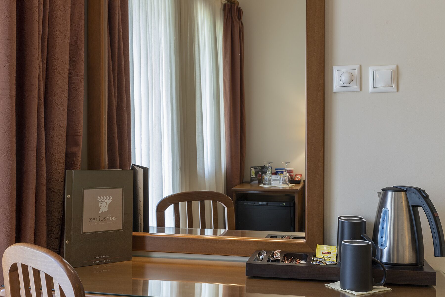 Een hotelkamer met een houten tafel, een stoel, een koffiezetapparaat en een spiegel die de kamer weerkaatst.