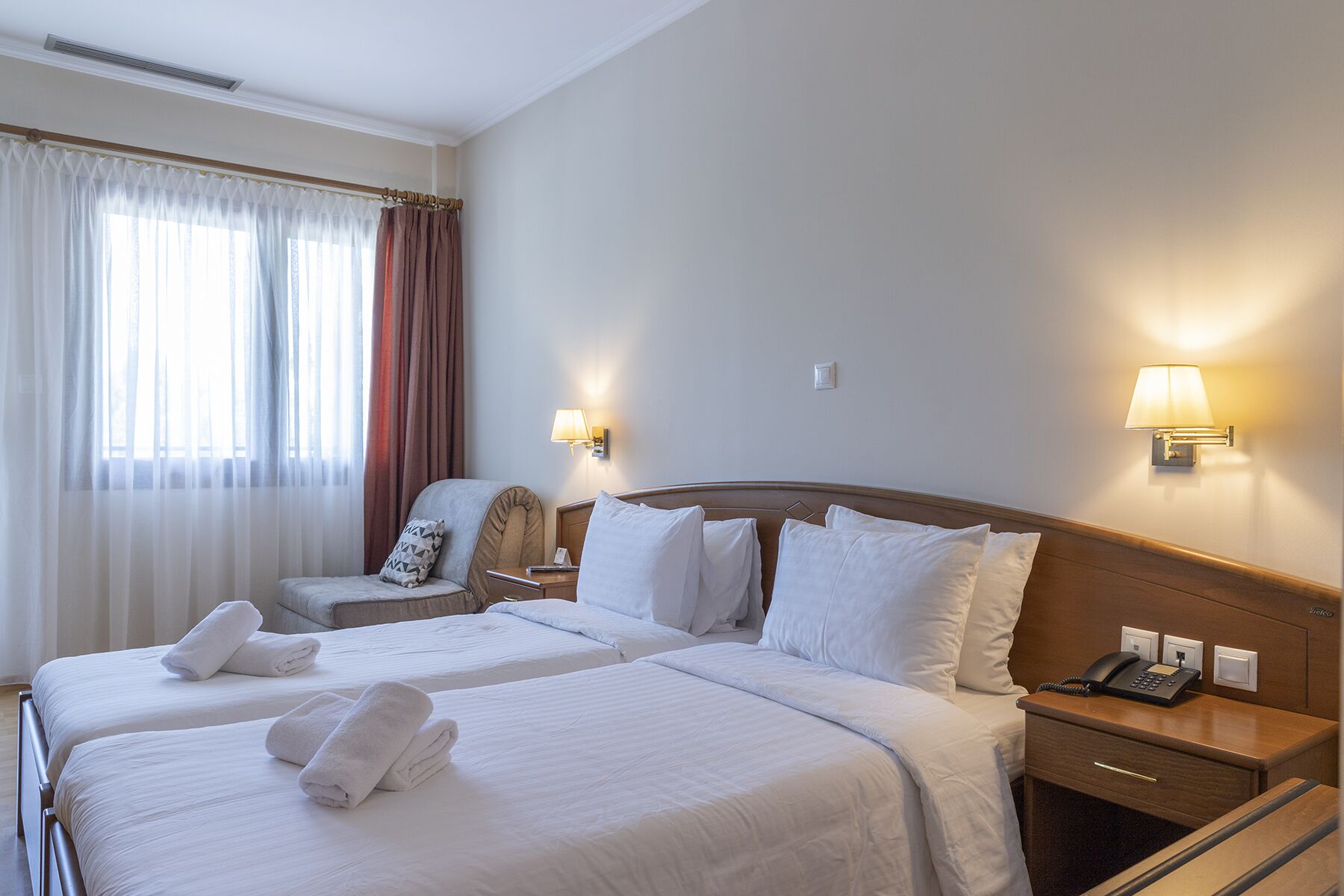 Habitación de hotel con dos camas, una silla, una mesita de noche con lámpara y un teléfono.