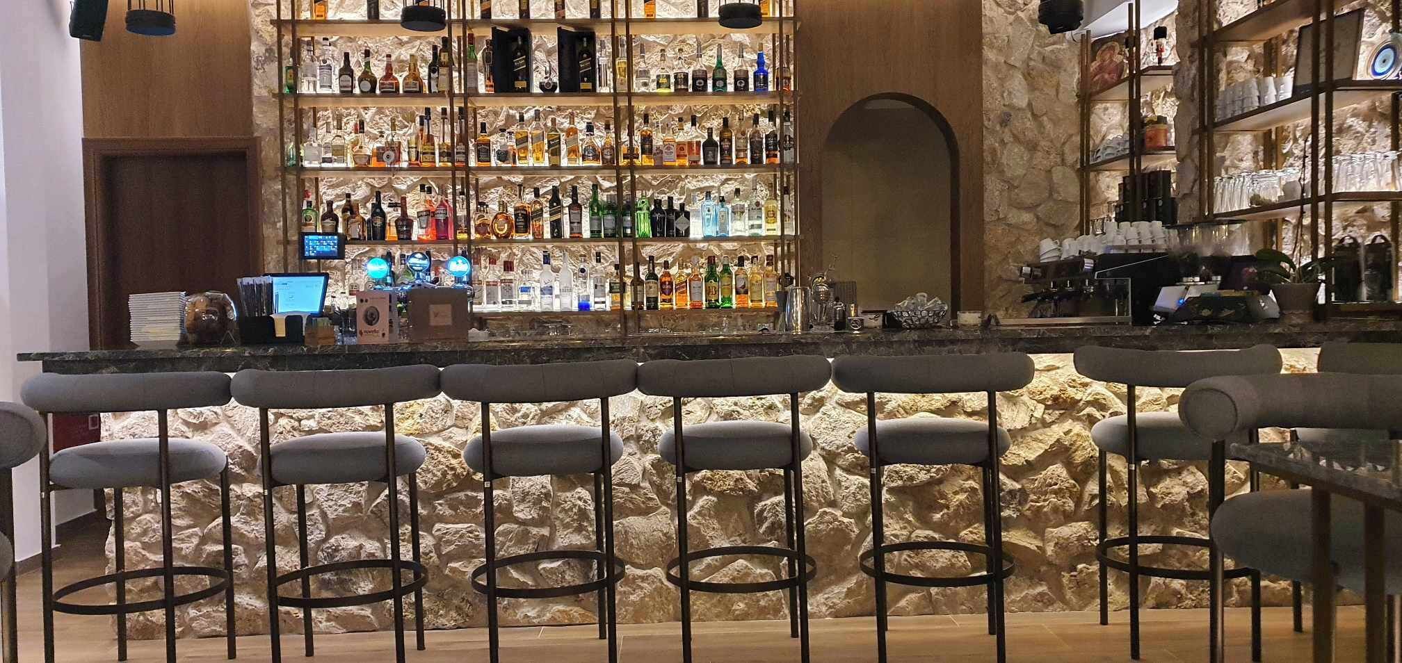 Un espace bar doté de nombreux tabourets, d’une étagère bien garnie de bouteilles et d’un mur en pierre en arrière-plan.
