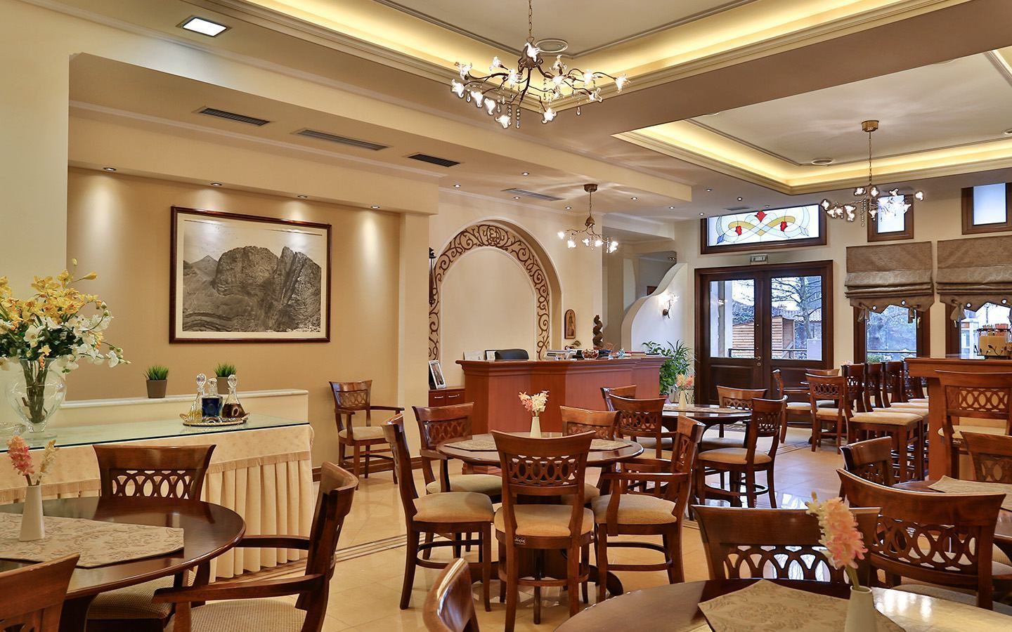 En hotellobby med flere spiseborde og stole, et receptionsområde og en lysekrone.