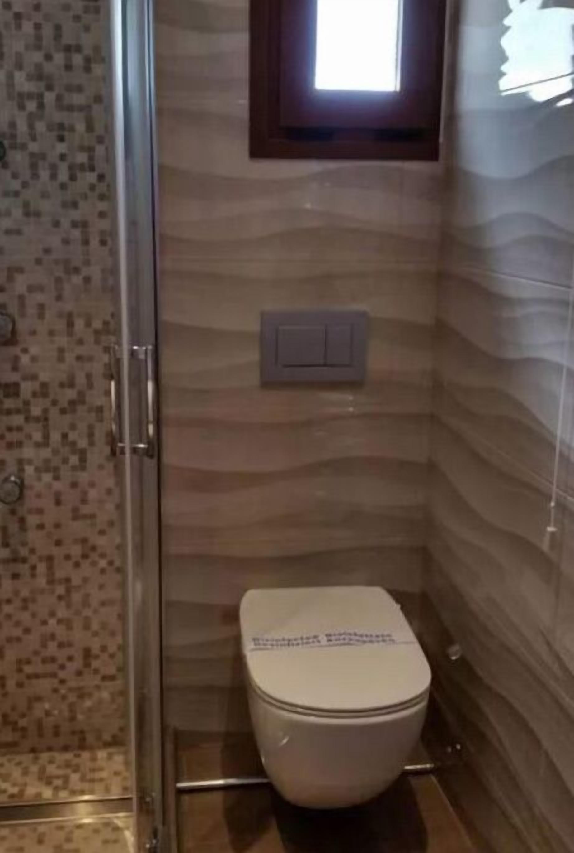 A small bathroom with a toilet, a shower, and a window.