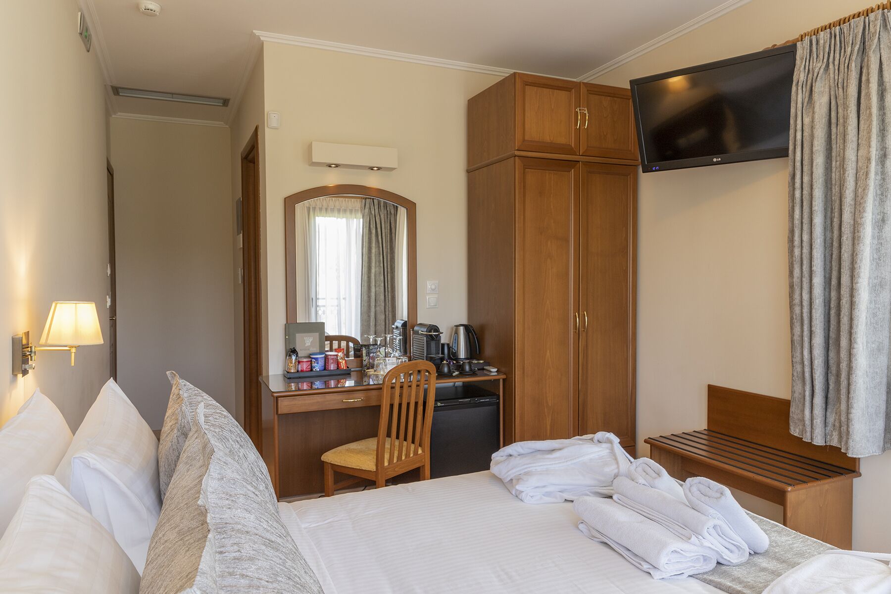Quarto de hotel com cama, escrivaninha com espelho, televisão e guarda-roupa.