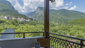 A balcony with a table and chair, overlooking a mountainous landscape with a village in the distance. - Xenios Dias Boutique Hotel (Dio-Olympos)