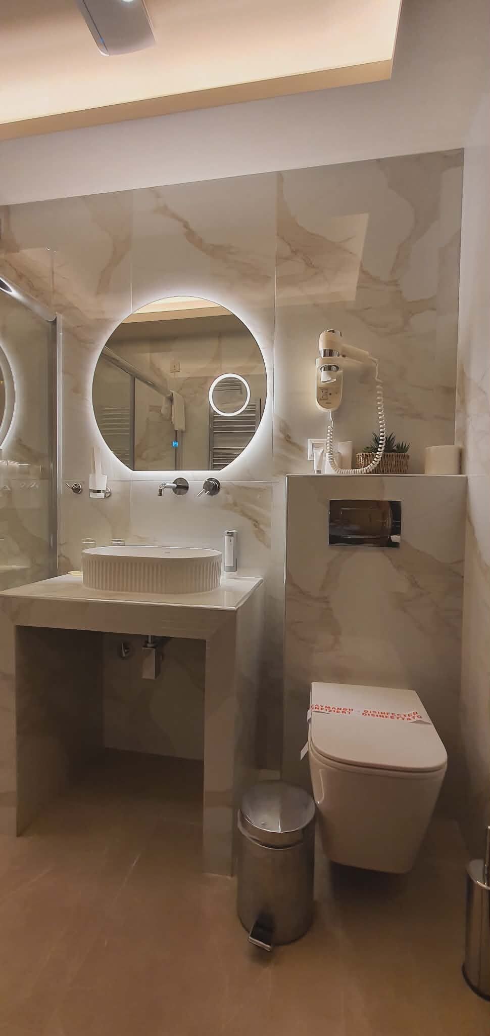 A modern bathroom with a round mirror, a sink, a toilet, and a hairdryer.