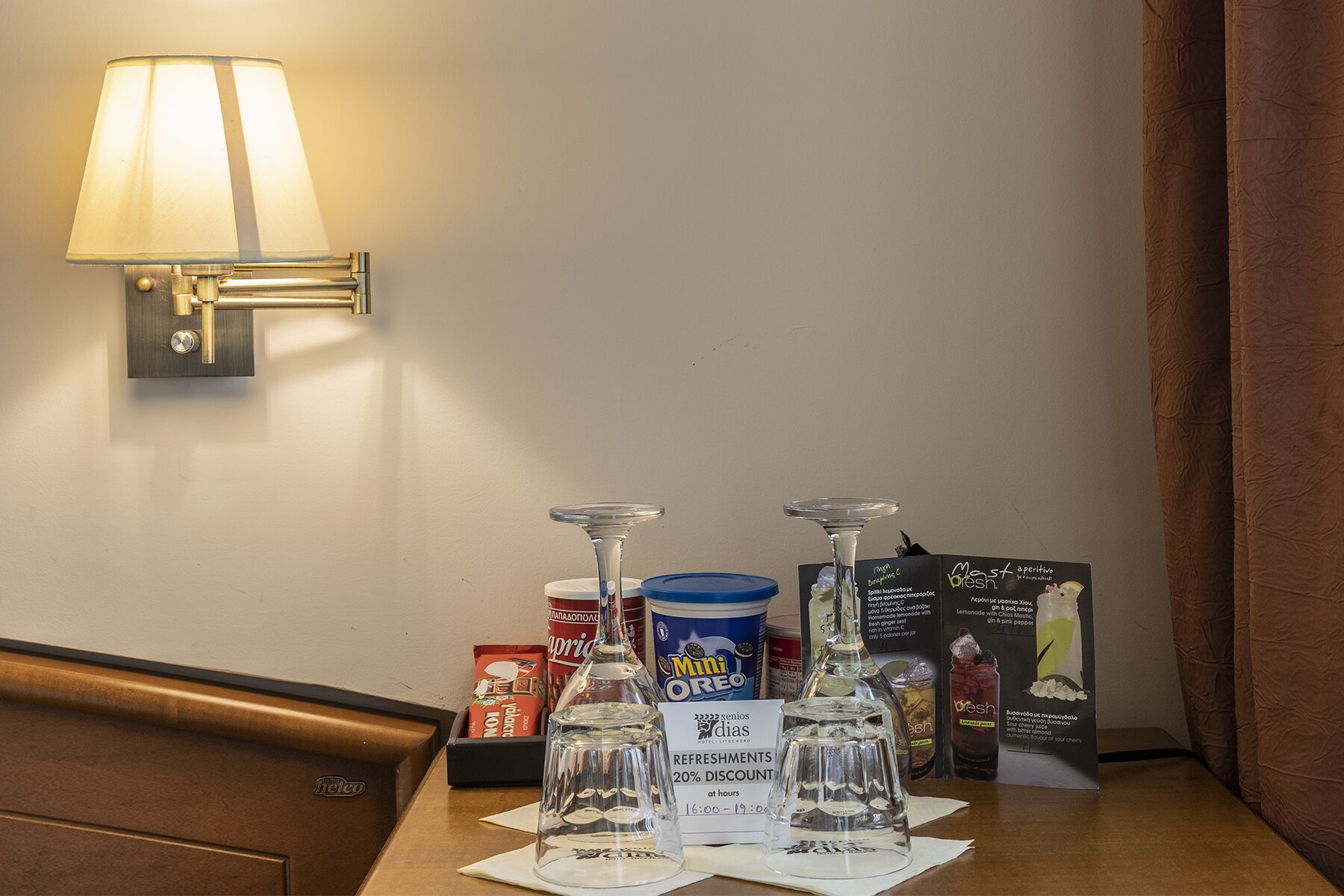 A hotel minibar with a lamp, a Mini Oreo container, and various refreshment bottles.