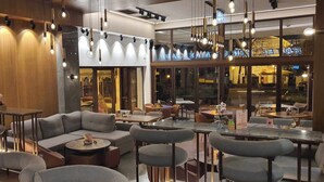 A modern restaurant interior with a mix of seating options including a sofa, round tables, and chairs. - Xenios Dias Boutique Hotel (Dio-Olympos)