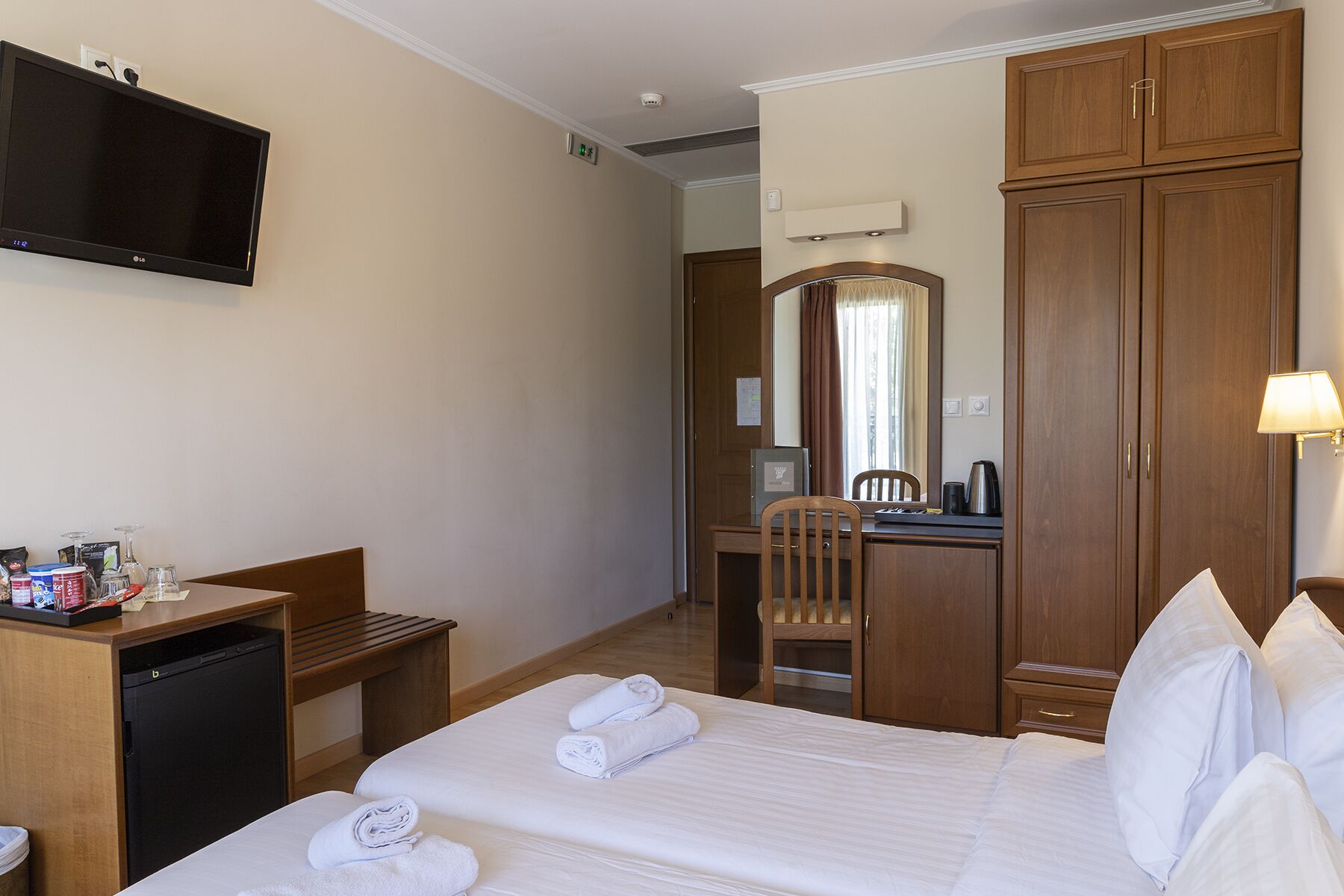 Una habitación de hotel con cama, escritorio, silla, televisor y armario.