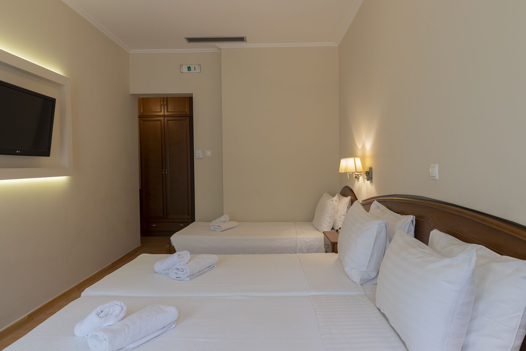 Ein Hotelzimmer mit zwei Betten, einem an der Wand befestigten Fernseher, einem Kleiderschrank und einer Nachttischlampe.