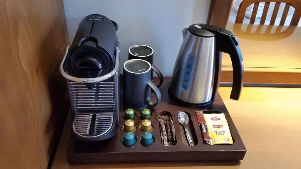 Una cafetera, dos tazas, un hervidor y una bandeja con utensilios y sobres de té Lipton.