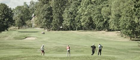 A golf course with a flag, trees, and a few people.