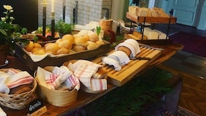 Una mesa de buffet con panes y pasteles diversos, velas y un ambiente rústico con manteles de madera.