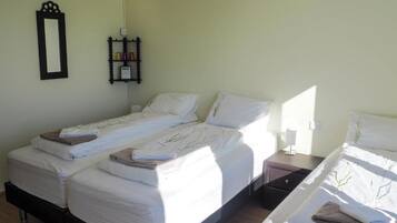 A hotel room with two single beds, a bedside table with a lamp, a small shelf with toiletries, and a wall-mounted mirror.