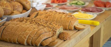 A variety of breads and pastries on a wooden table, with a yellow rolling pin nearby.
