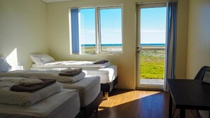 Habitación de hotel con dos camas, un escritorio y vistas a la playa a través de amplias ventanas.