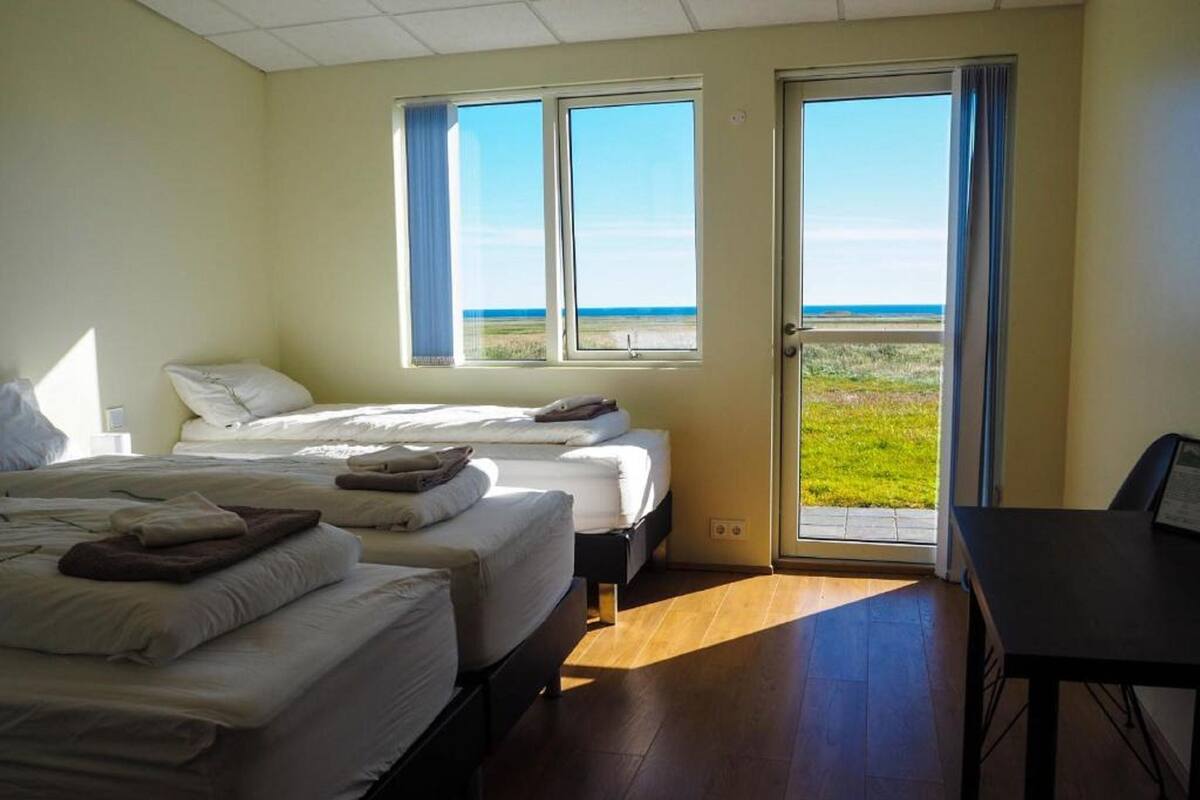 Une chambre d’hôtel avec deux lits, un bureau et une vue sur la plage grâce à de grandes fenêtres.