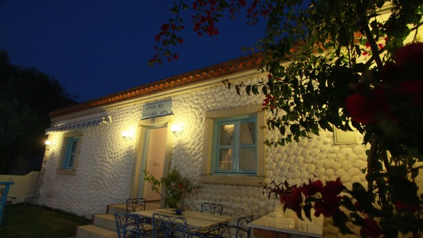 A stone building with a sign, a table with chairs, and a brick wall. - Cakirbey Otel (Cesme)