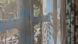 A room with a window covered by a mesh screen, a floral curtain, and a view of the outdoors. - Cakirbey Otel (Cesme)