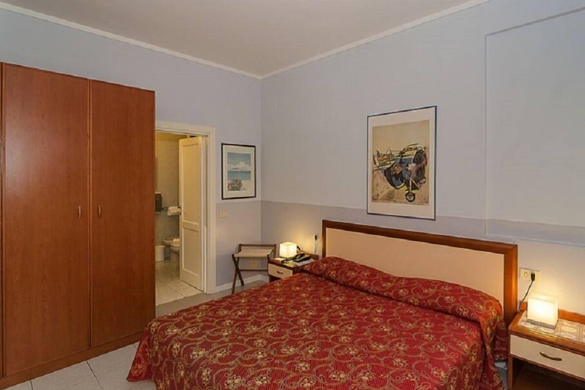 Een slaapkamer met een groot bed, een houten garderobe, een nachtkastje met een lamp en een lijst met een afbeelding aan de muur.