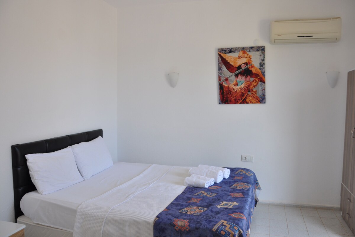 A hotel room with a bed, a wall-mounted air conditioner, and a painting.