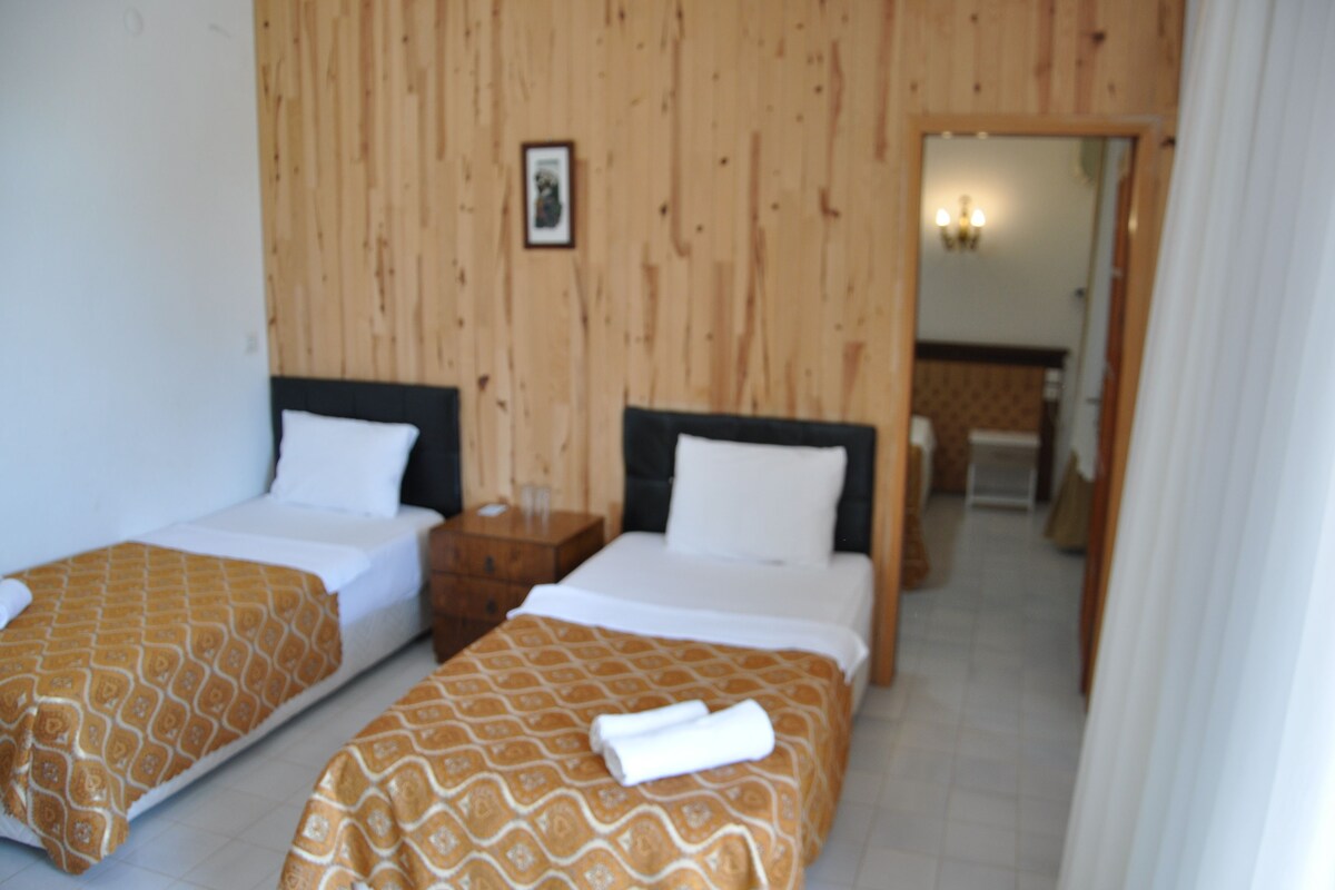 A hotel room with two beds, wooden panel walls, a small bedside table, and a bathroom visible through an open door.