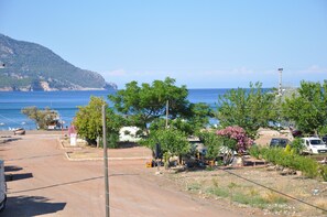 A coastal road with a dirt path, parked vehicles, and a small building with a sign. - ADRASAN SHAMBALA (Kumluca)