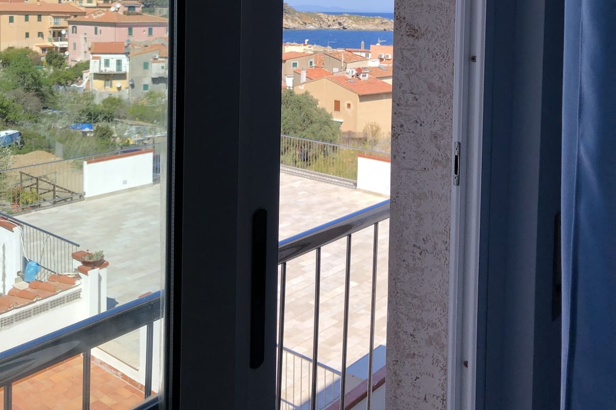 A view from a balcony with a clear sky, a distant coastline, and buildings in the background.