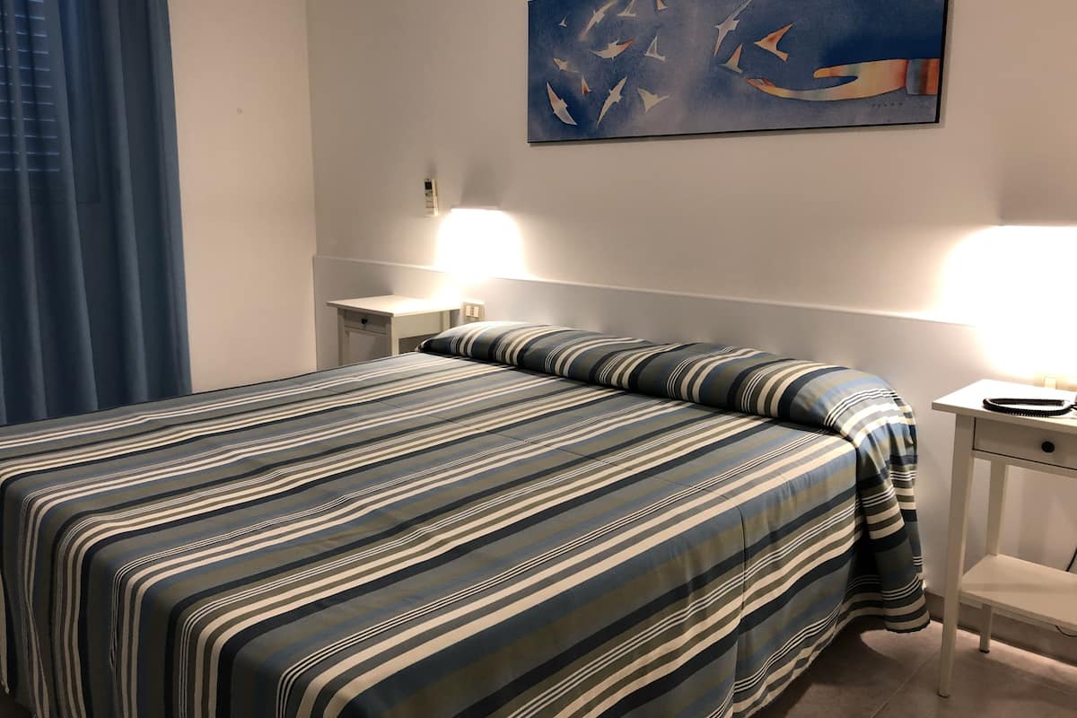 A hotel room with a bed, a nightstand, a lamp, and a painting on the wall.