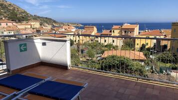 A terrace with a view of a coastal town, including buildings with red-tiled roofs and a clear blue sky.