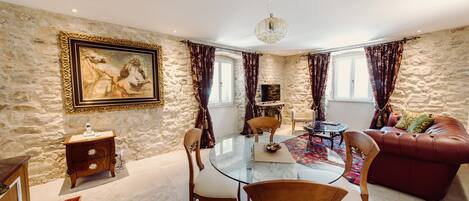 A spacious living room with a stone wall, a glass coffee table, leather sofa, and a painting.