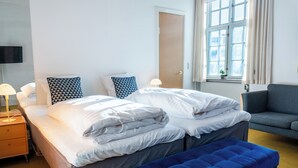 A hotel room with a bed, a bench, a sofa, a TV, and a window with curtains. - Palads Hotel (Viborg)