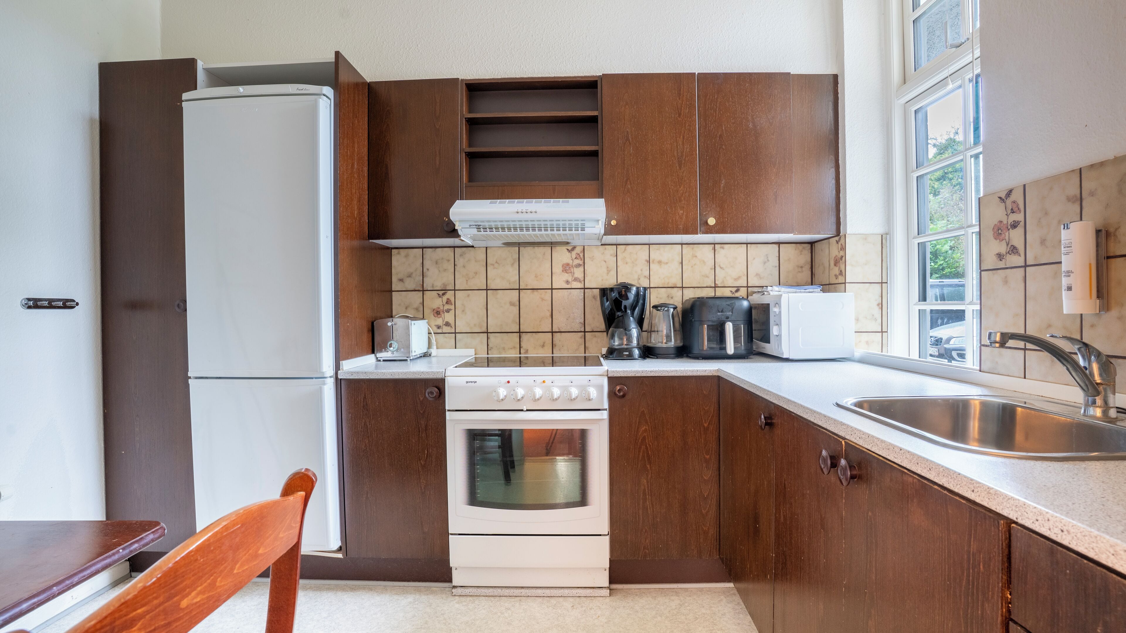 A compact kitchen with wooden cabinets, a white refrigerator, a stove, a coffee maker, and a toaster.