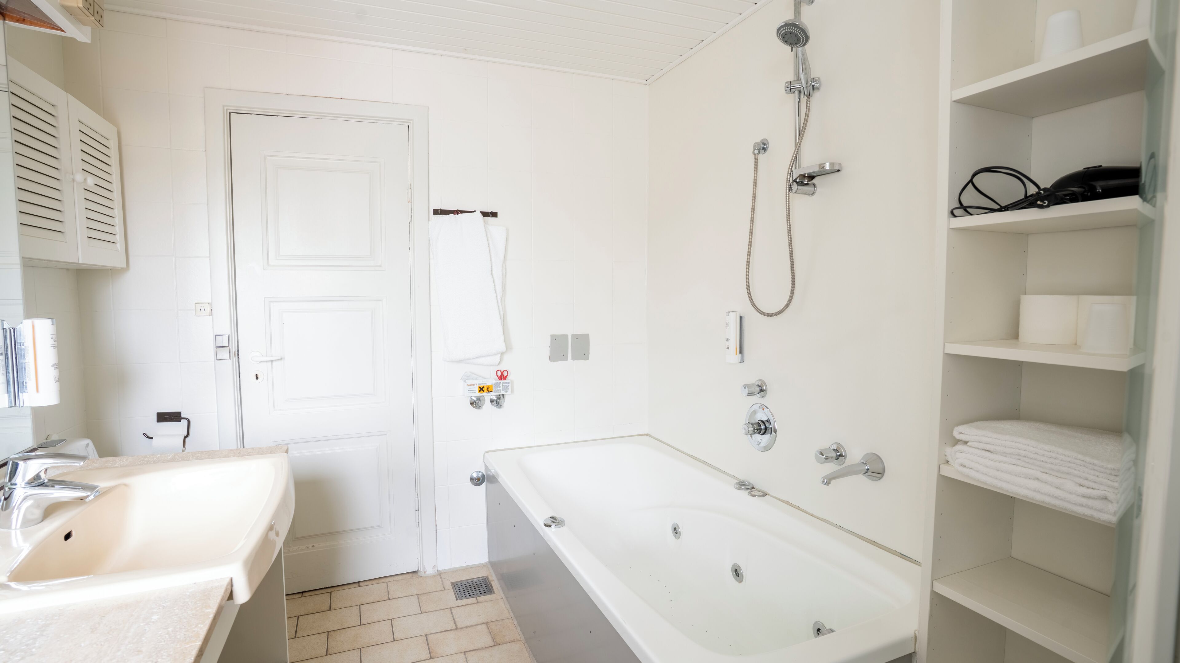 A bathroom with a sink, toilet, and bathtub. There are shelves with towels and toiletries.