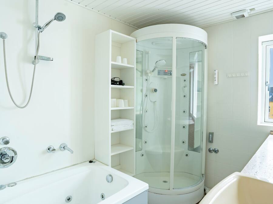 Un baño moderno con ducha de vidrio, una bañera blanca y una ventana con vista a edificios.