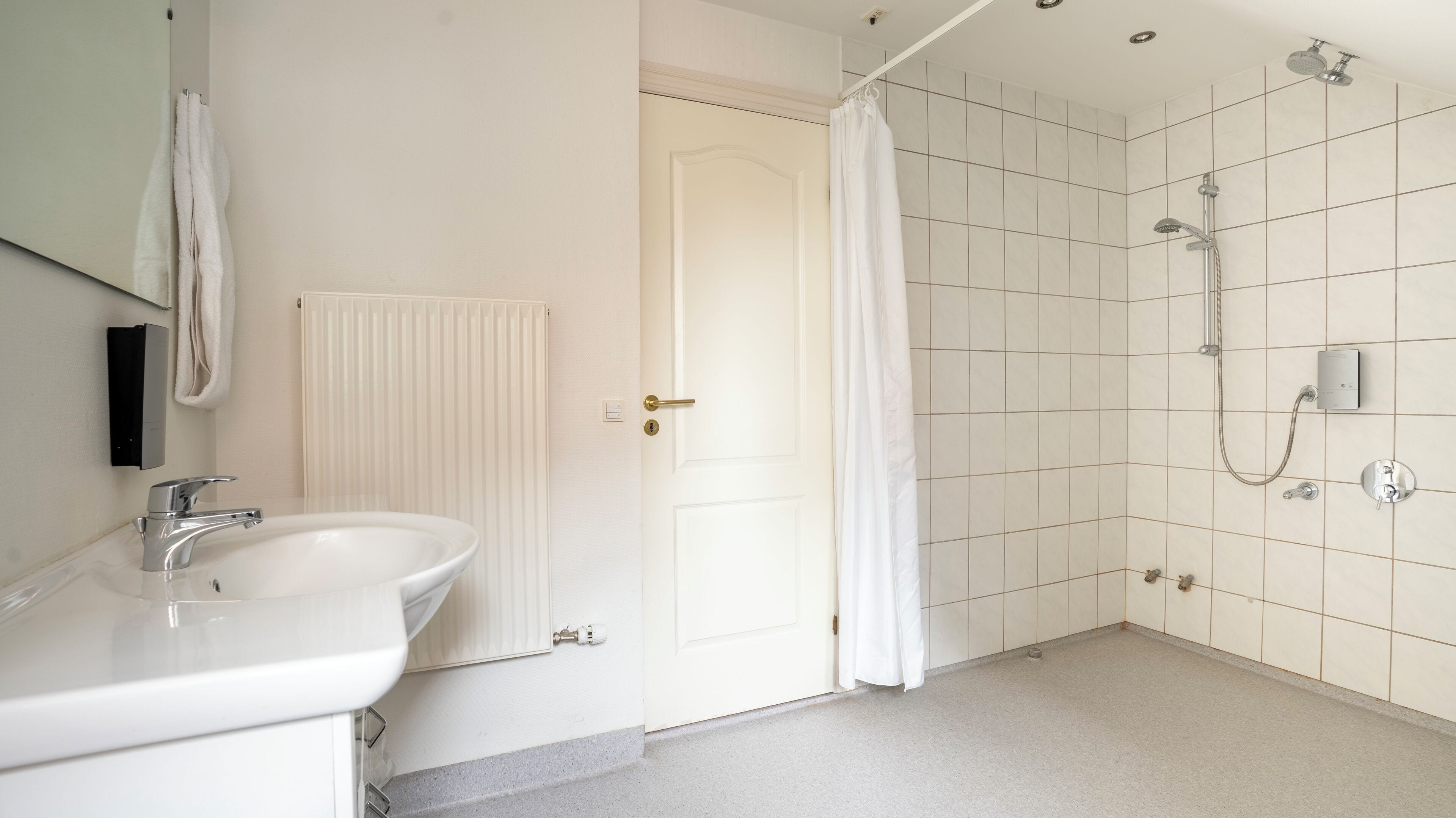A bathroom with a white sink, a shower with a glass door, and a white radiator.