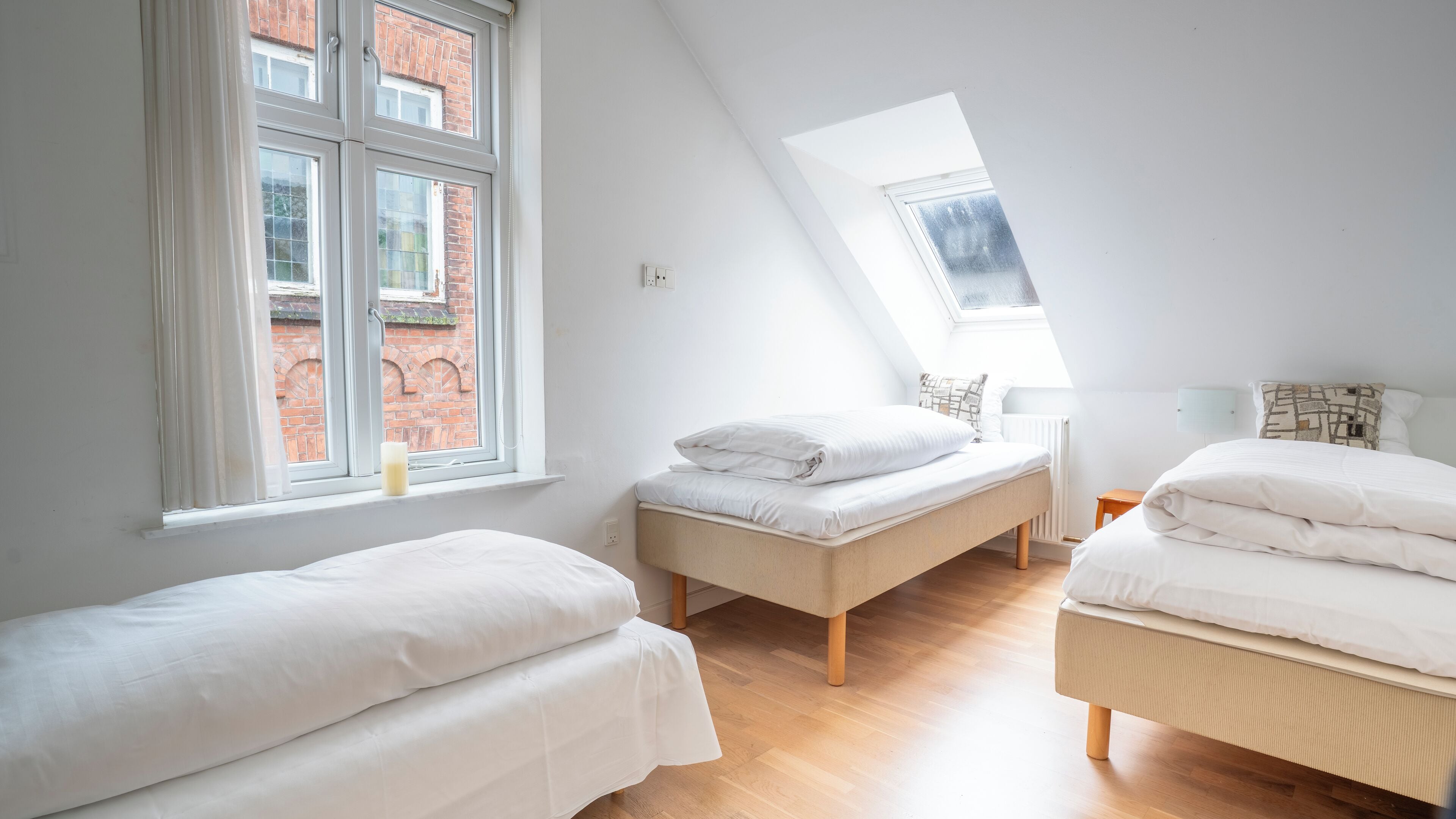 A bedroom with two beds, a skylight, and a view of a brick building.