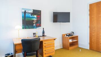 Una habitación con un escritorio de madera, una silla, un televisor montado en la pared y una estantería.