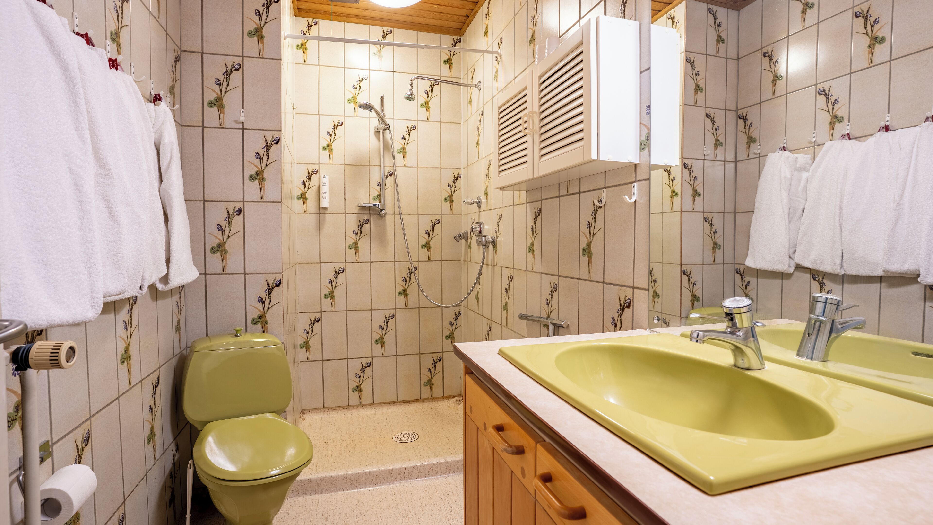 Casa de banho com lavatório amarelo, toalhas brancas e sanita.