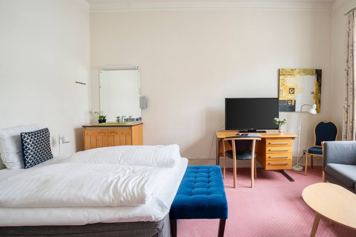A hotel room with a bed, a desk with a computer, a sofa, and a window with curtains.