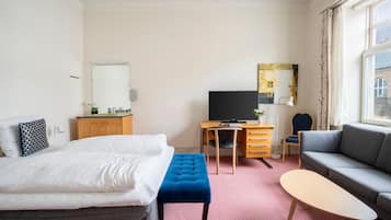 Een hotelkamer met een bed, een bureau met computer, een bank en een raam met gordijnen.