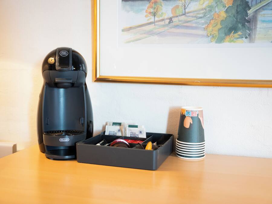 Une machine à café, un plateau avec des dosettes de café et une tasse, et un tableau encadré accroché au mur.