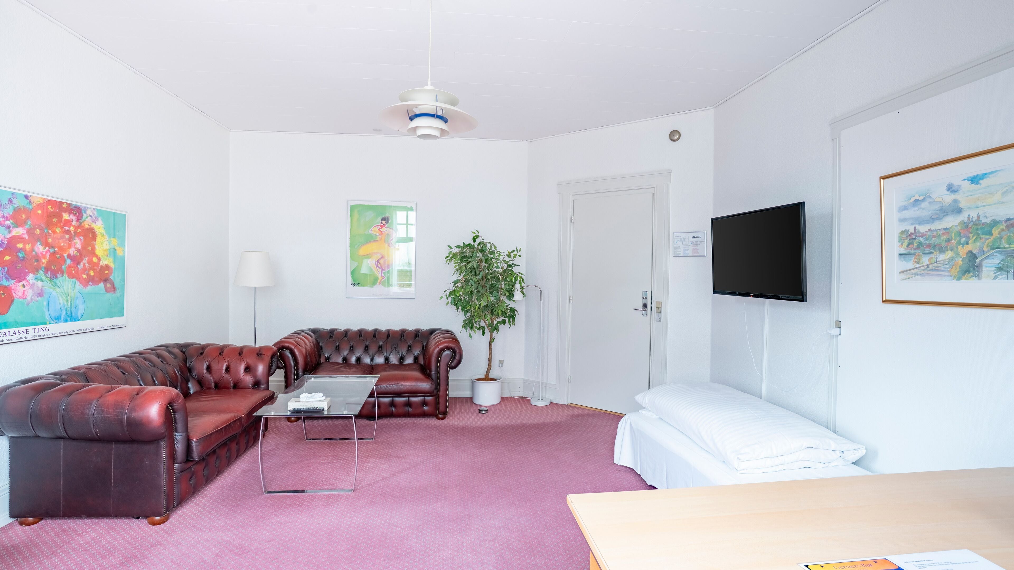 A living room with a leather sofa, a coffee table, a potted plant, a flat-screen TV, and artwork on the walls.
