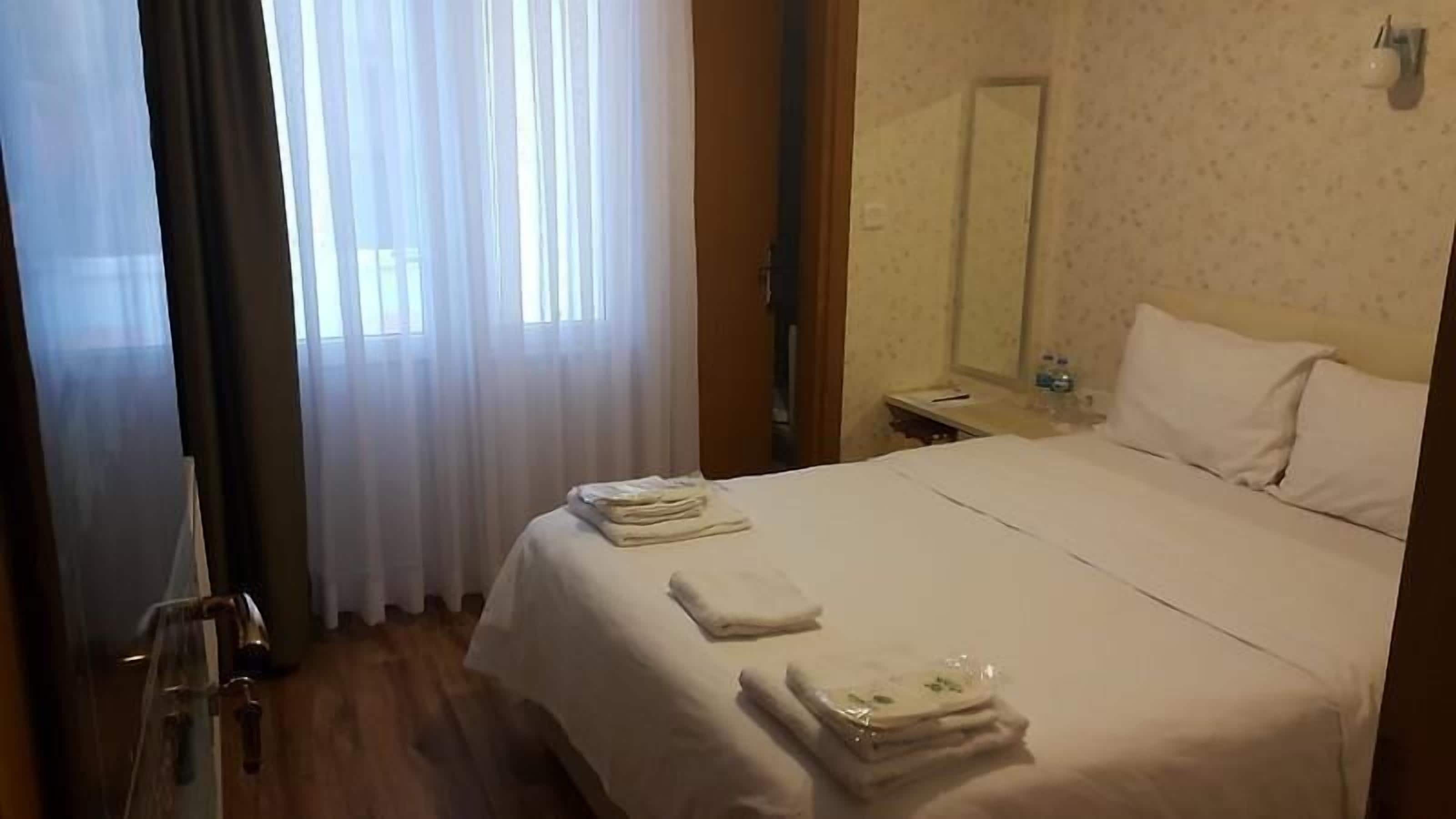 A hotel room with a bed, a nightstand, a mirror, and a window with curtains.