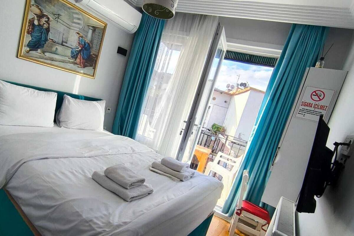 Une chambre d’hôtel avec un lit, un tableau, une fenêtre avec des rideaux et un panneau sur le mur.