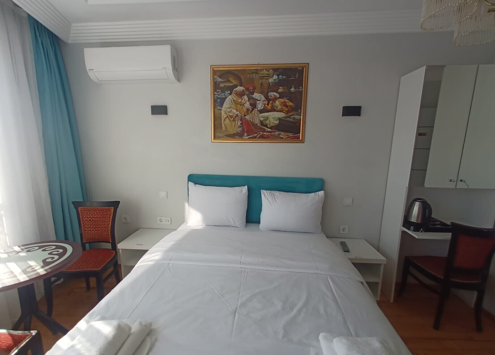 A hotel room with a bed, a desk, a chair, a table, and a painting on the wall.