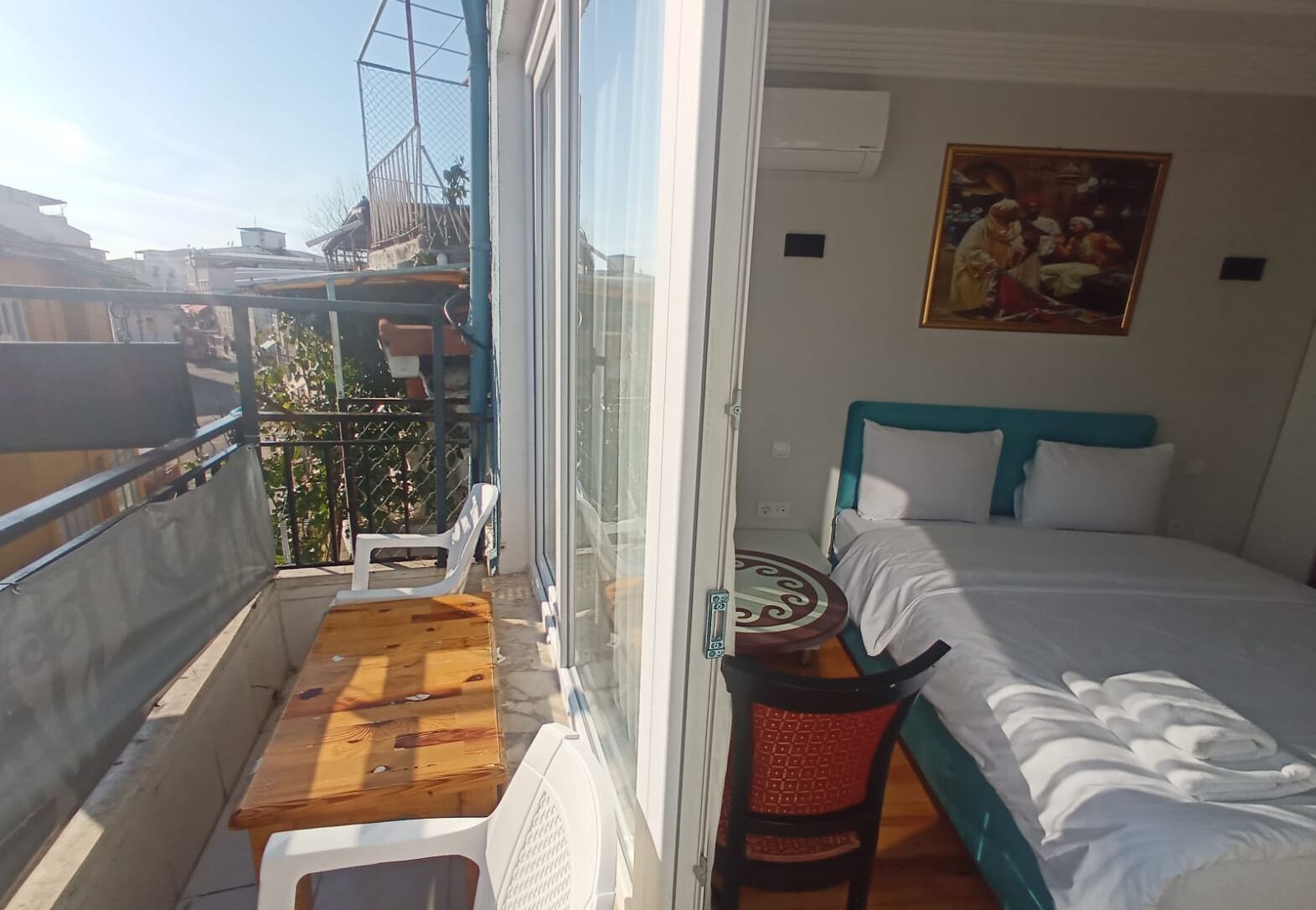 Un balcón con una mesa y sillas de madera, una cama con ropa de cama blanca y azul, y un cuadro en la pared.
