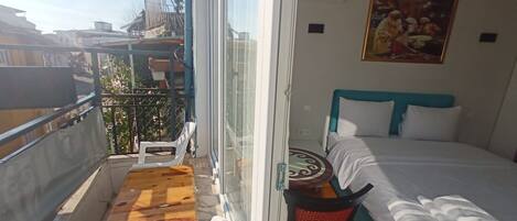 Un balcón con una mesa y sillas de madera, una cama con ropa de cama blanca y azul, y un cuadro en la pared.