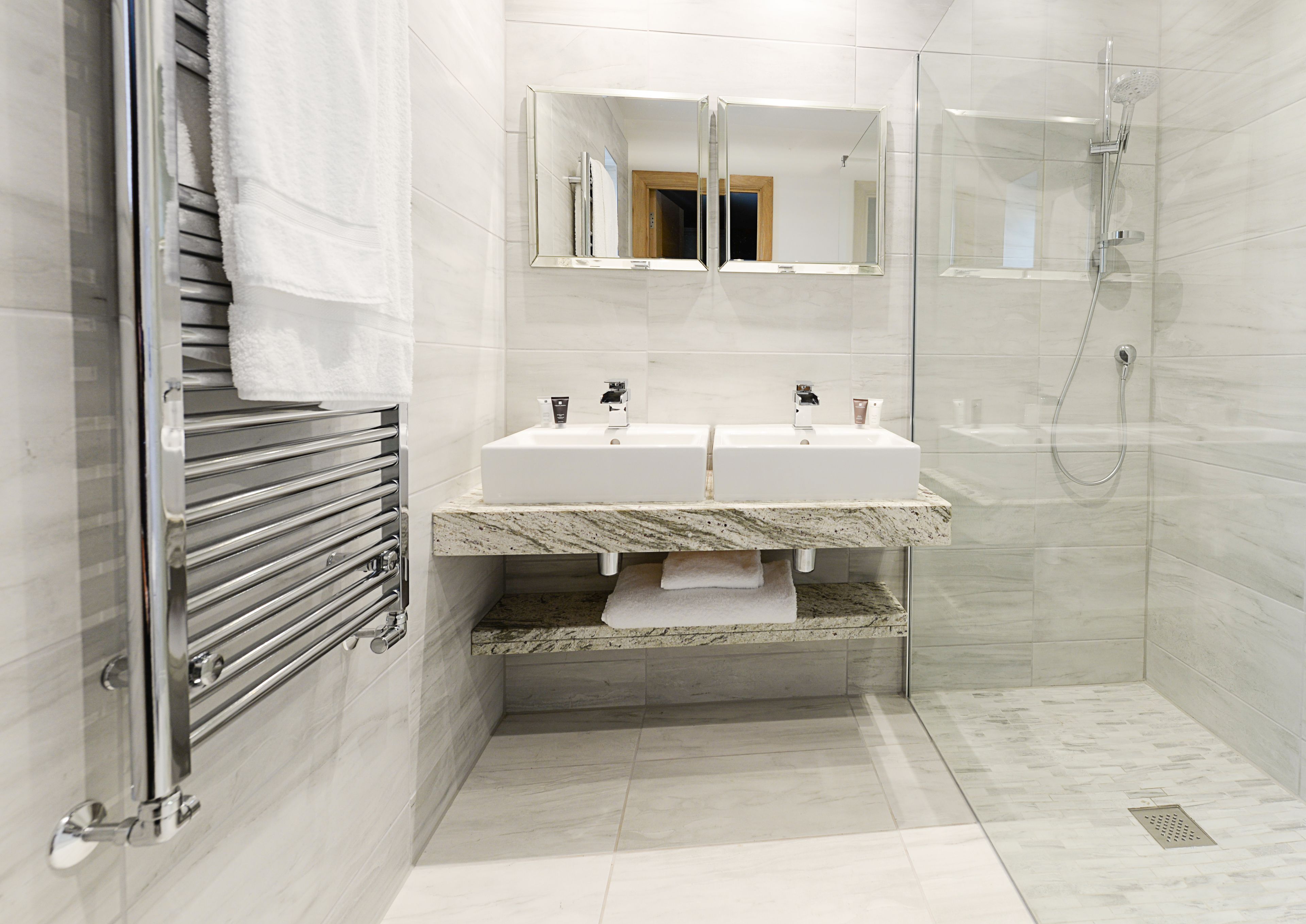 Un baño moderno con lavamanos doble, cabina de ducha de vidrio y toallero.