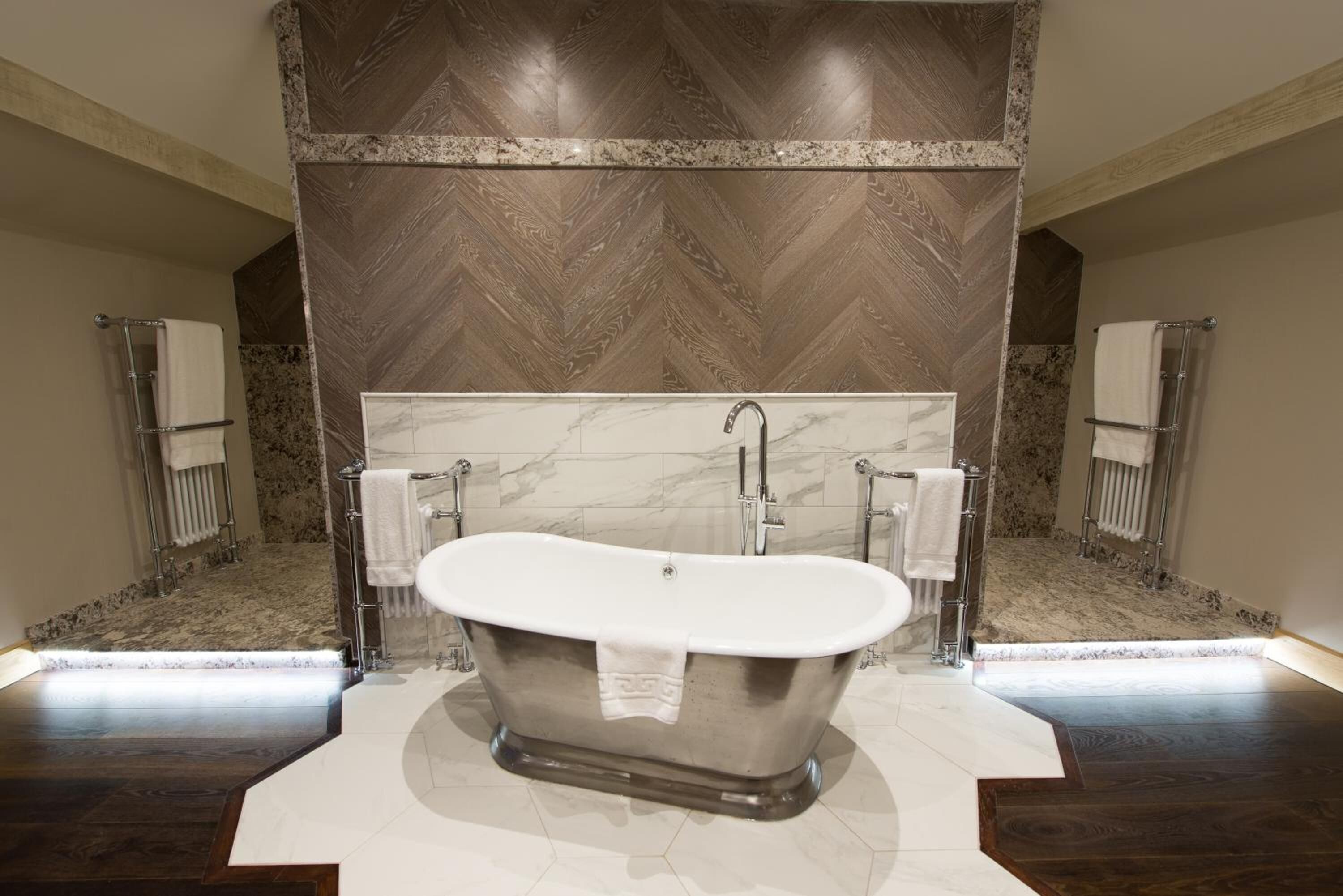 Une salle de bain moderne avec une baignoire îlot, des murs en marbre et un motif de parquet en chevrons sur le mur supérieur.