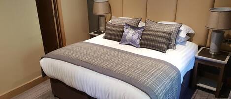 A neatly made bed with a checkered bedspread, two bedside lamps, and a headboard.
