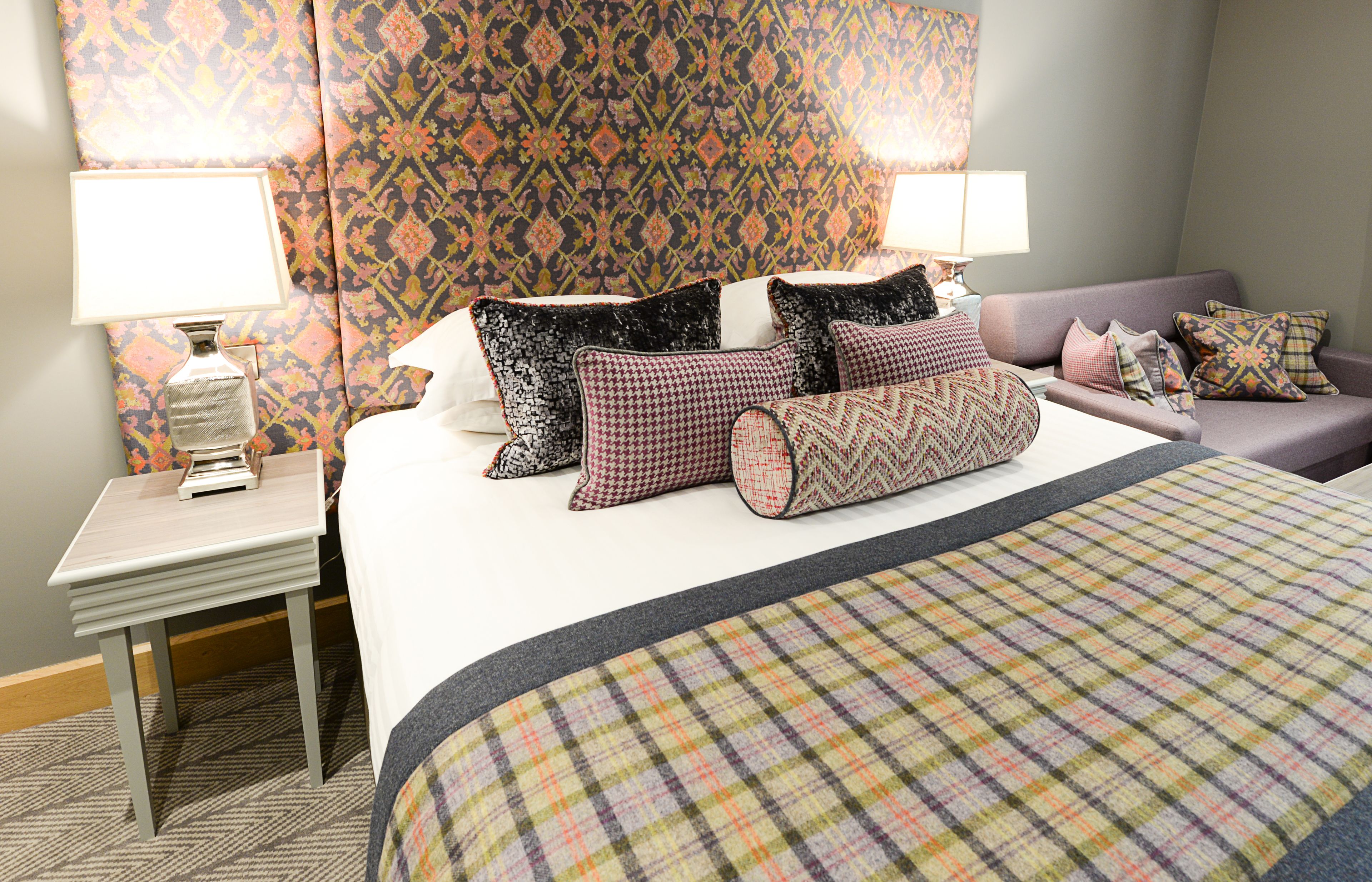 Una habitación de hotel con una cama, una mesita de noche, una lámpara y un cabecero estampado.